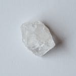 A detailed close-up of a rough clear quartz crystal, unpolished and natural on a white surface.